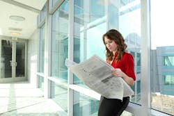 woman in professional attire reading a newspaper while leaning against a wall of window woman in professional attire reading a newspaper while leaning against a wall of window