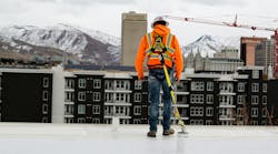 worker standing on a ledge tethered with fall protection PPE overlooking housing complex and mountains worker standing on a ledge tethered with fall protection PPE overlooking housing complex and mountains