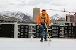 worker standing on a ledge tethered with fall protection PPE overlooking housing complex and mountains worker standing on a ledge tethered with fall protection PPE overlooking housing complex and mountains