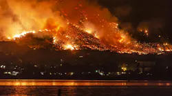 photo of a body of water in the forefront and a wildfire burning in the distance