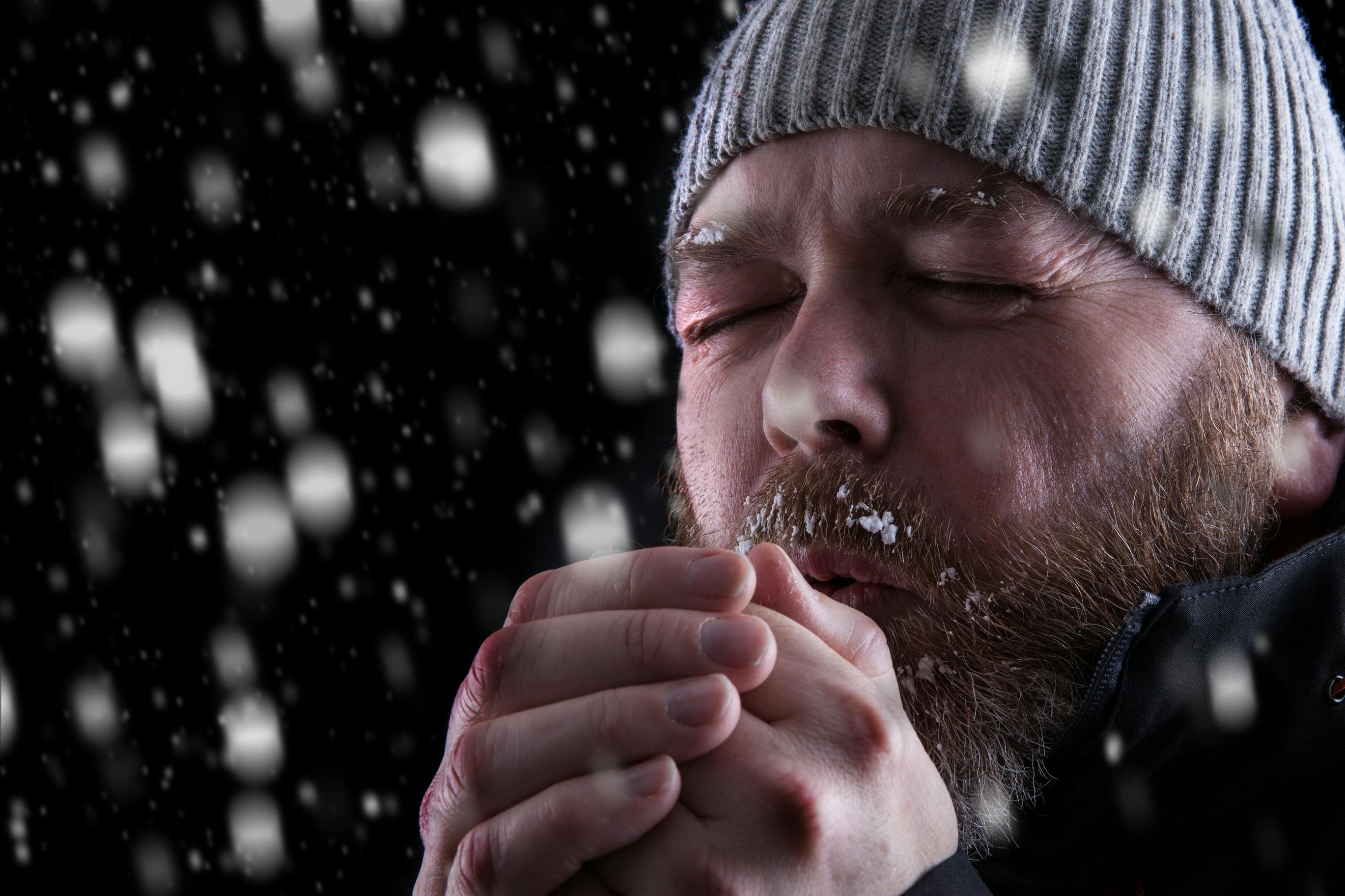 Man wearing a hat and coat shivering in the cold