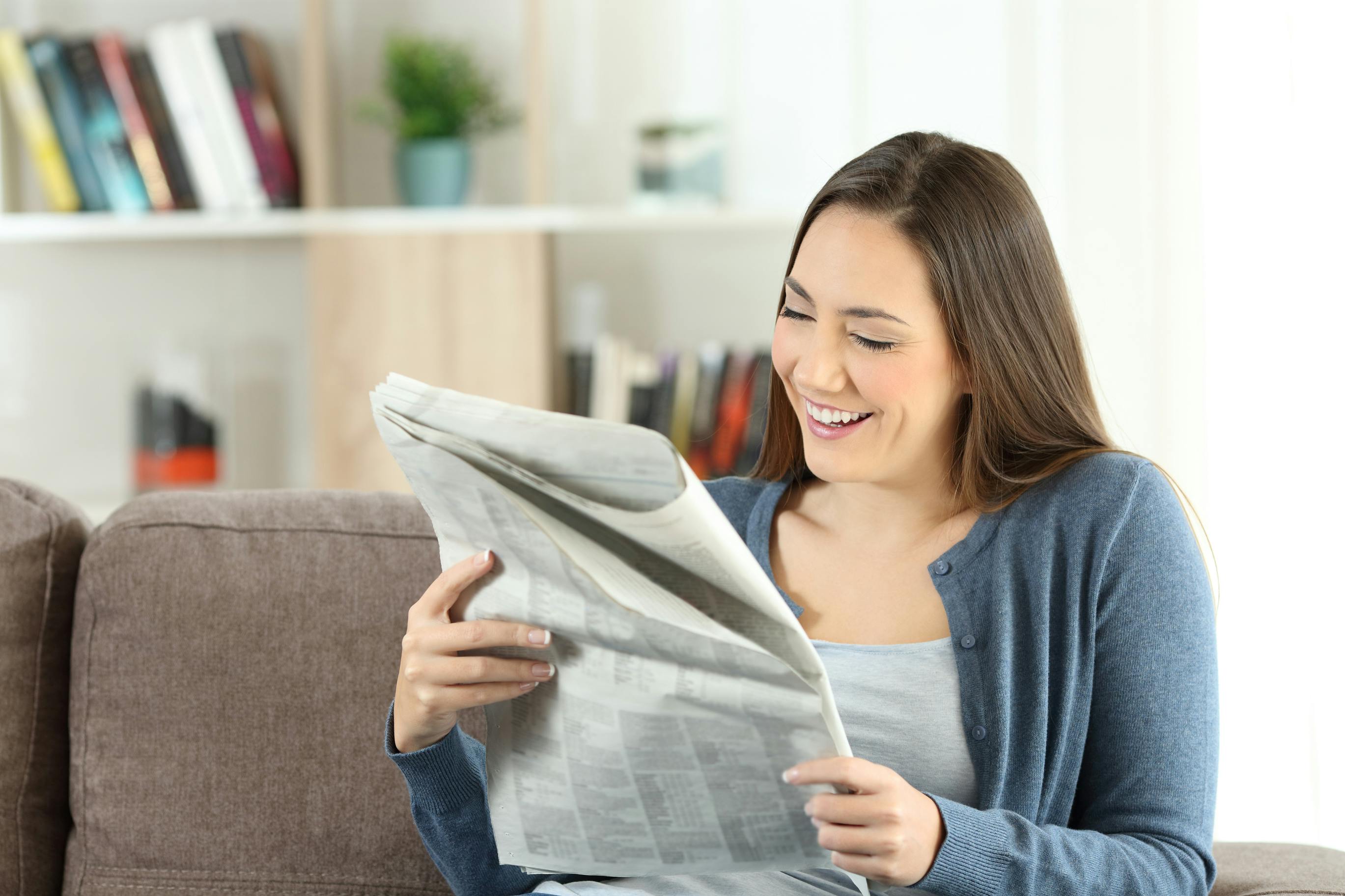 woman sitting on a couch reading a newspaper