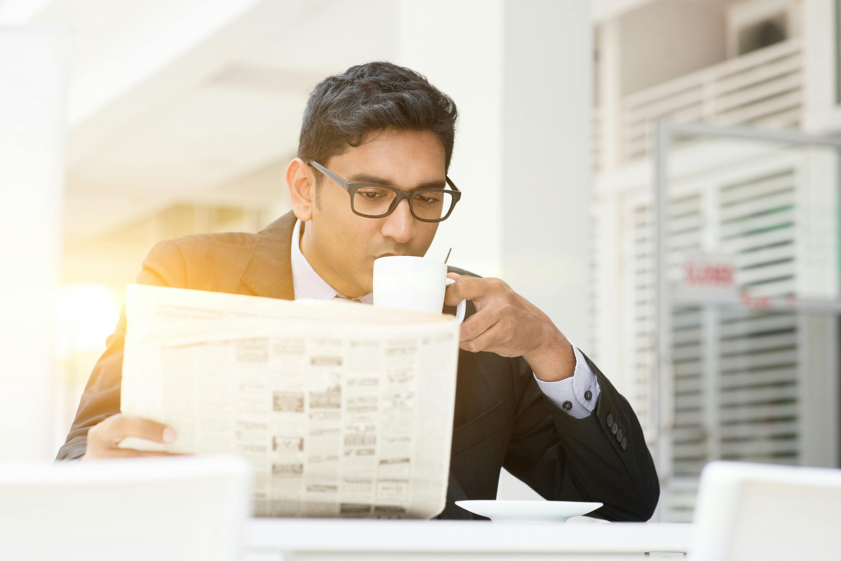 man in business suit drinking coffee and reading a newspaper