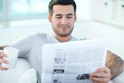 younger man reading newspaper on couch holding coffee mug younger man reading newspaper on couch holding coffee mug