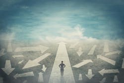 Profile of a woman looking ahead, standing on top of an arrow pointed straight ahead. She is surrounded by arrows in a scattering of directions, suggesting that she is continuing on her path ahead despite the chaos and uncertainty around her. Profile of a woman looking ahead, standing on top of an arrow pointed straight ahead. She is surrounded by arrows in a scattering of directions, suggesting that she is continuing on her path ahead despite the chaos and uncertainty around her.