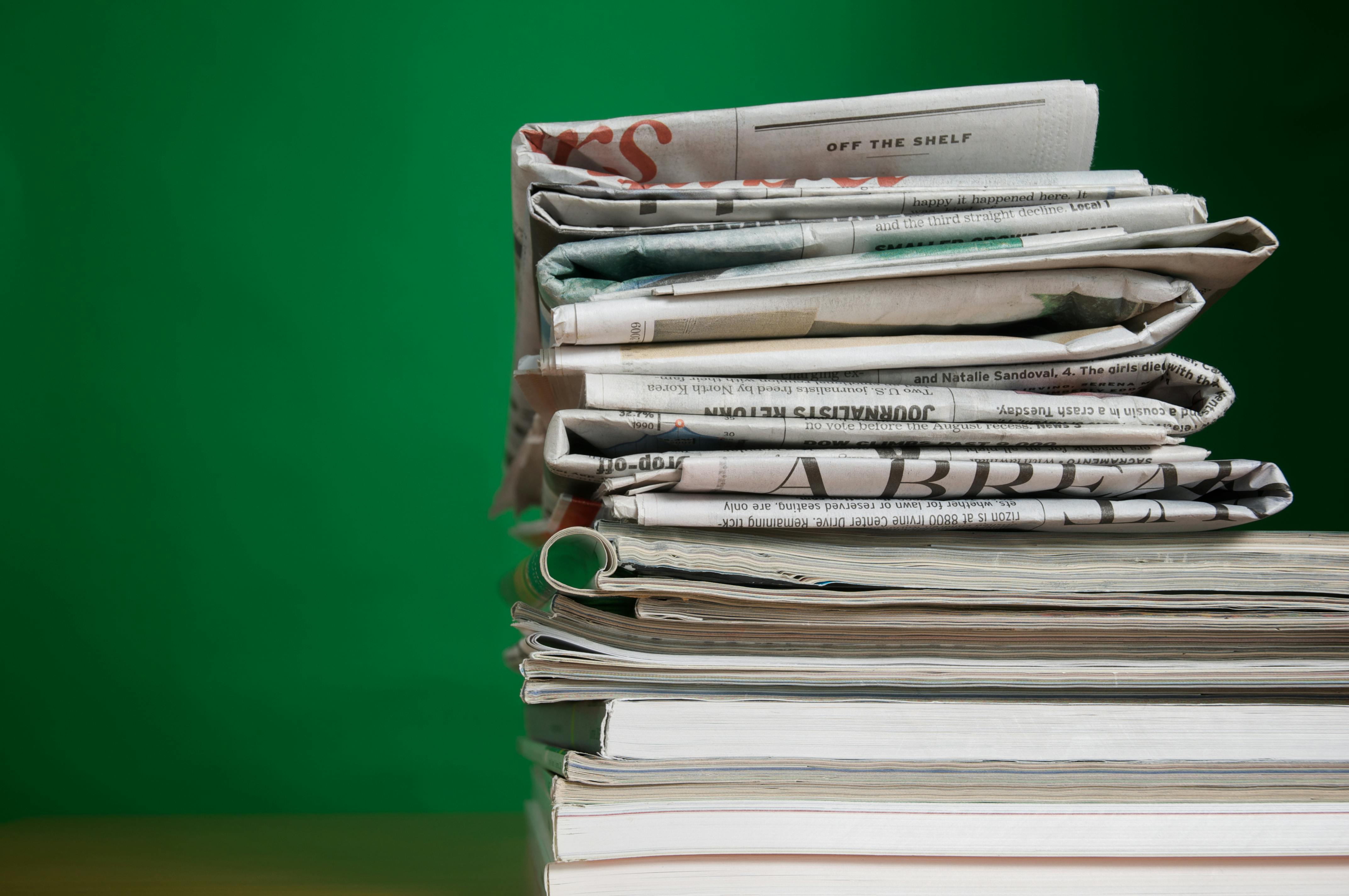 stack of newspapers and magazines against a green background