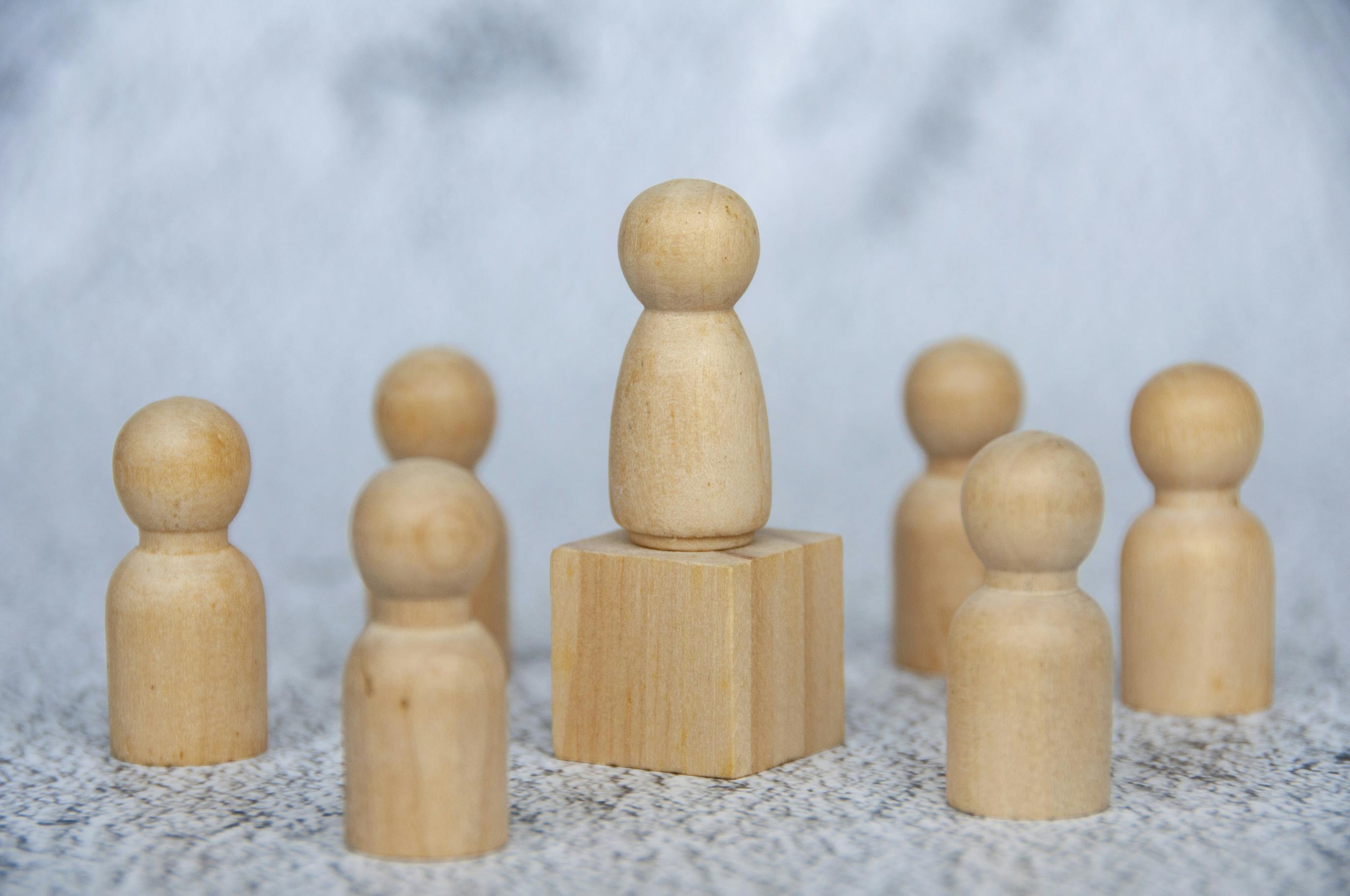 A wooden pawn on a block surrounded by other pawns. Thematic display of a leader surrounded by followers.