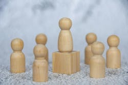 A wooden pawn on a block surrounded by other pawns. Thematic display of a leader surrounded by followers. A wooden pawn on a block surrounded by other pawns. Thematic display of a leader surrounded by followers.