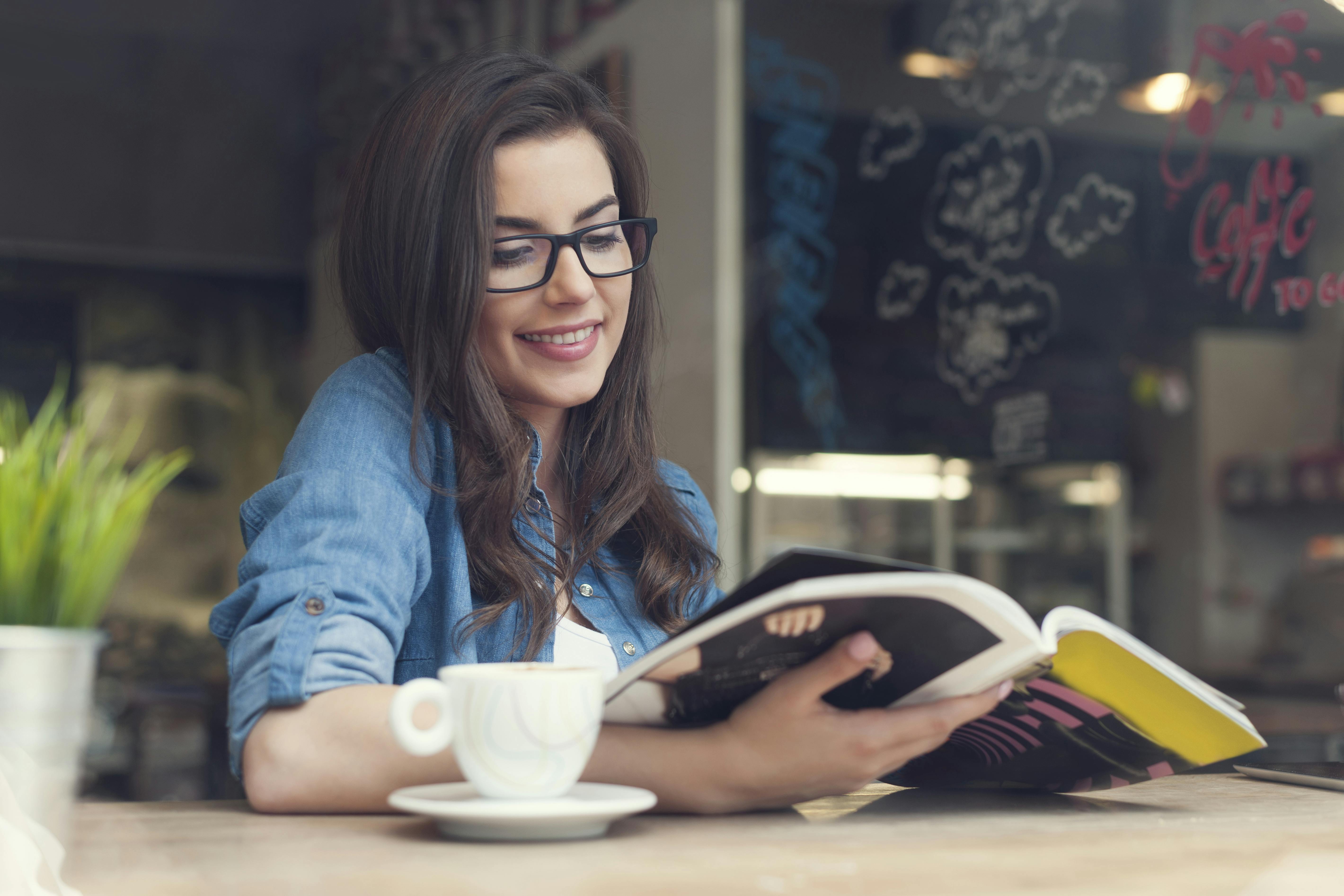woman sitting at a cafe reading a magazine and enjoying a beverage