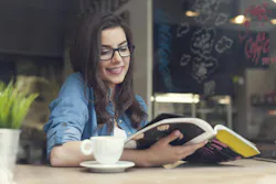 woman sitting at a cafe reading a magazine and enjoying a beverage woman sitting at a cafe reading a magazine and enjoying a beverage