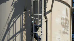 Photo of a worker climbing a caged ladder on the exterior of a metal structure