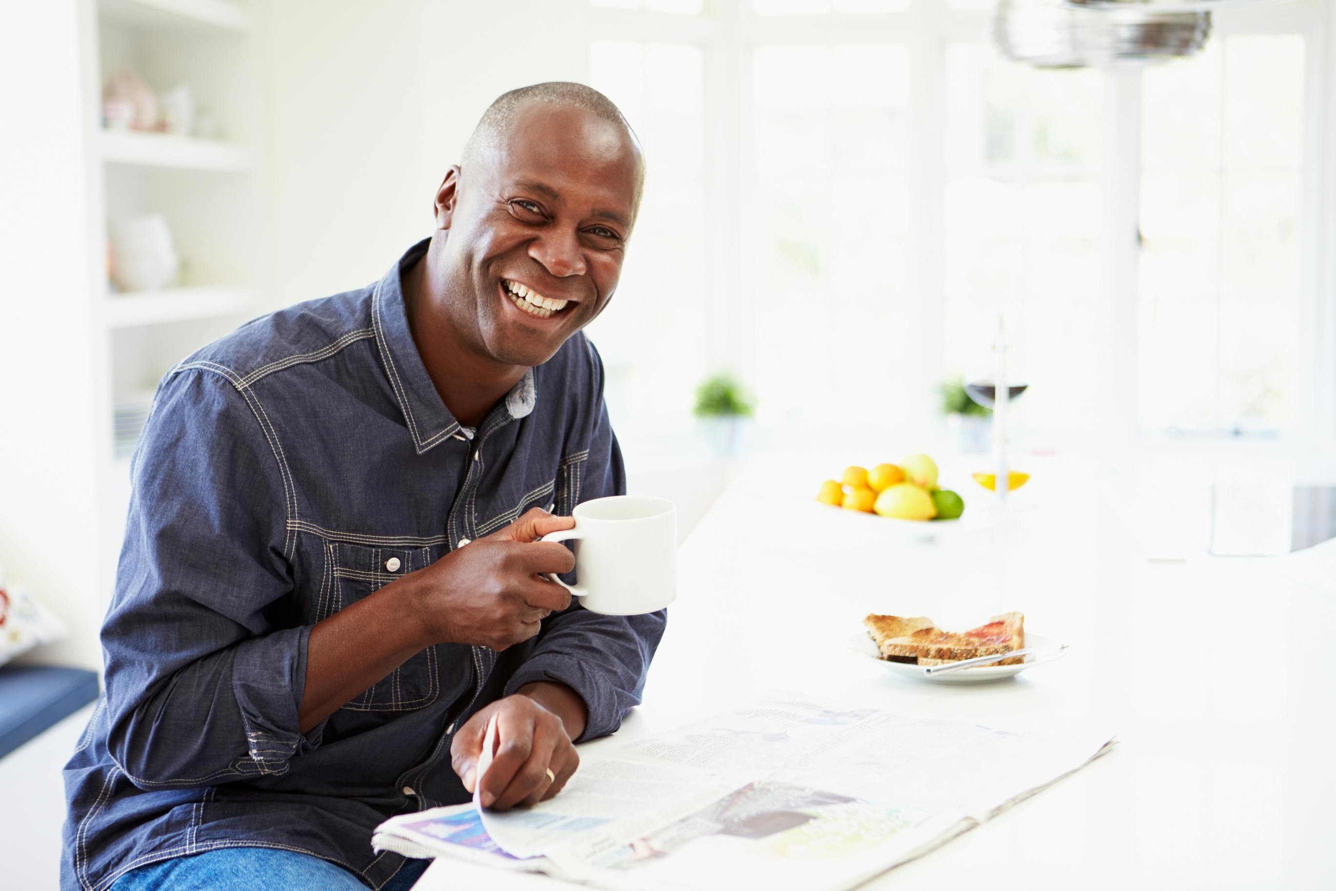 man smiling, drinking coffee and reading newspaper