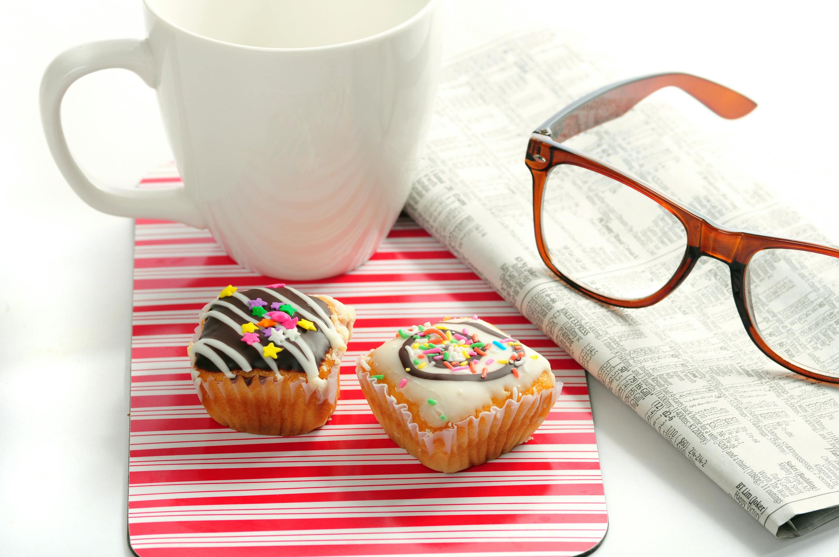 still photo of a newspaper, coffee mug, reading glasses and two pastries