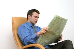 young man in a shirt, tie and dress slacks reading a newspaper in a beige leather desk chair young man in a shirt, tie and dress slacks reading a newspaper in a beige leather desk chair