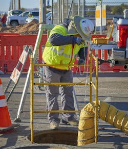 trade worker wearing a safety helmet and hi-visibility vest looking over barricaded manhole cover trade worker wearing a safety helmet and hi-visibility vest looking over barricaded manhole cover
