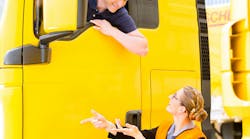 male truck driver in the cab talking to a woman wearing a safety vest on the ground male truck driver in the cab talking to a woman wearing a safety vest on the ground