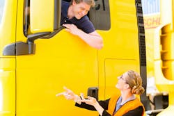 male truck driver in the cab talking to a woman wearing a safety vest on the ground male truck driver in the cab talking to a woman wearing a safety vest on the ground