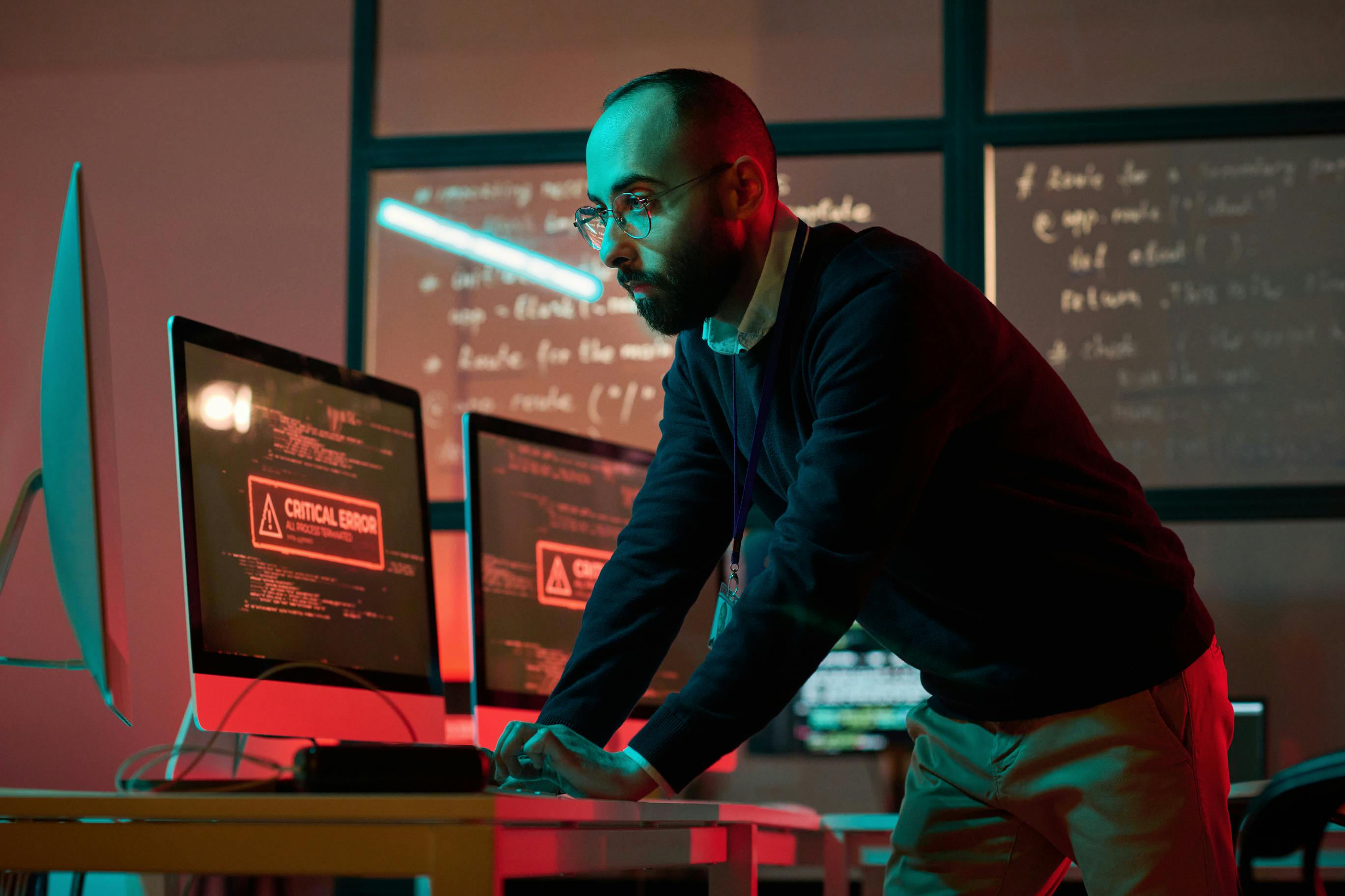 man standing and leaning over to look at computer screens that read 'Critical Error'