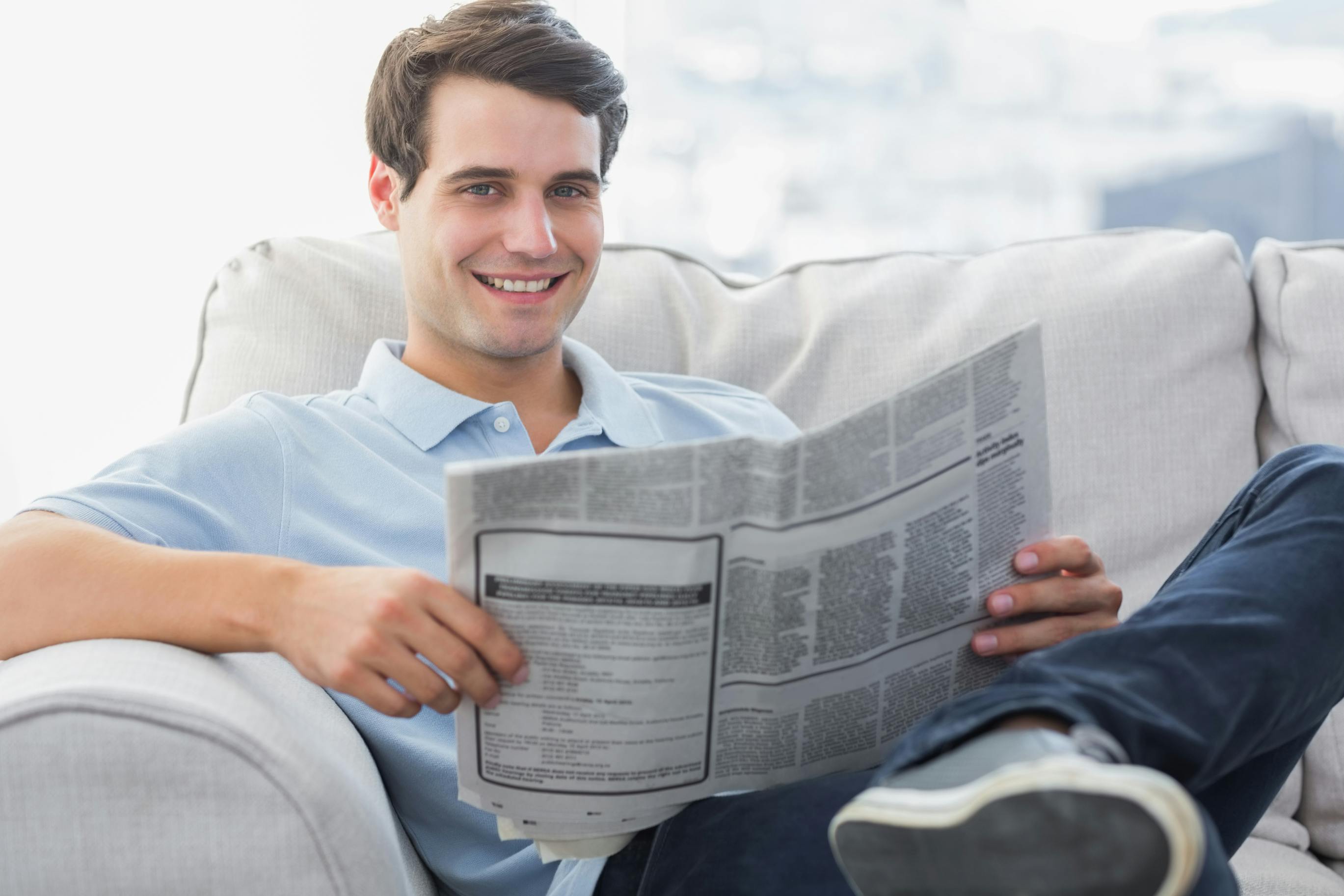 young man sitting on couch reading the newspaper