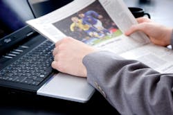 Image of someone in a suit coat reading the newspaper next to a laptop and coffee mug Image of someone in a suit coat reading the newspaper next to a laptop and coffee mug