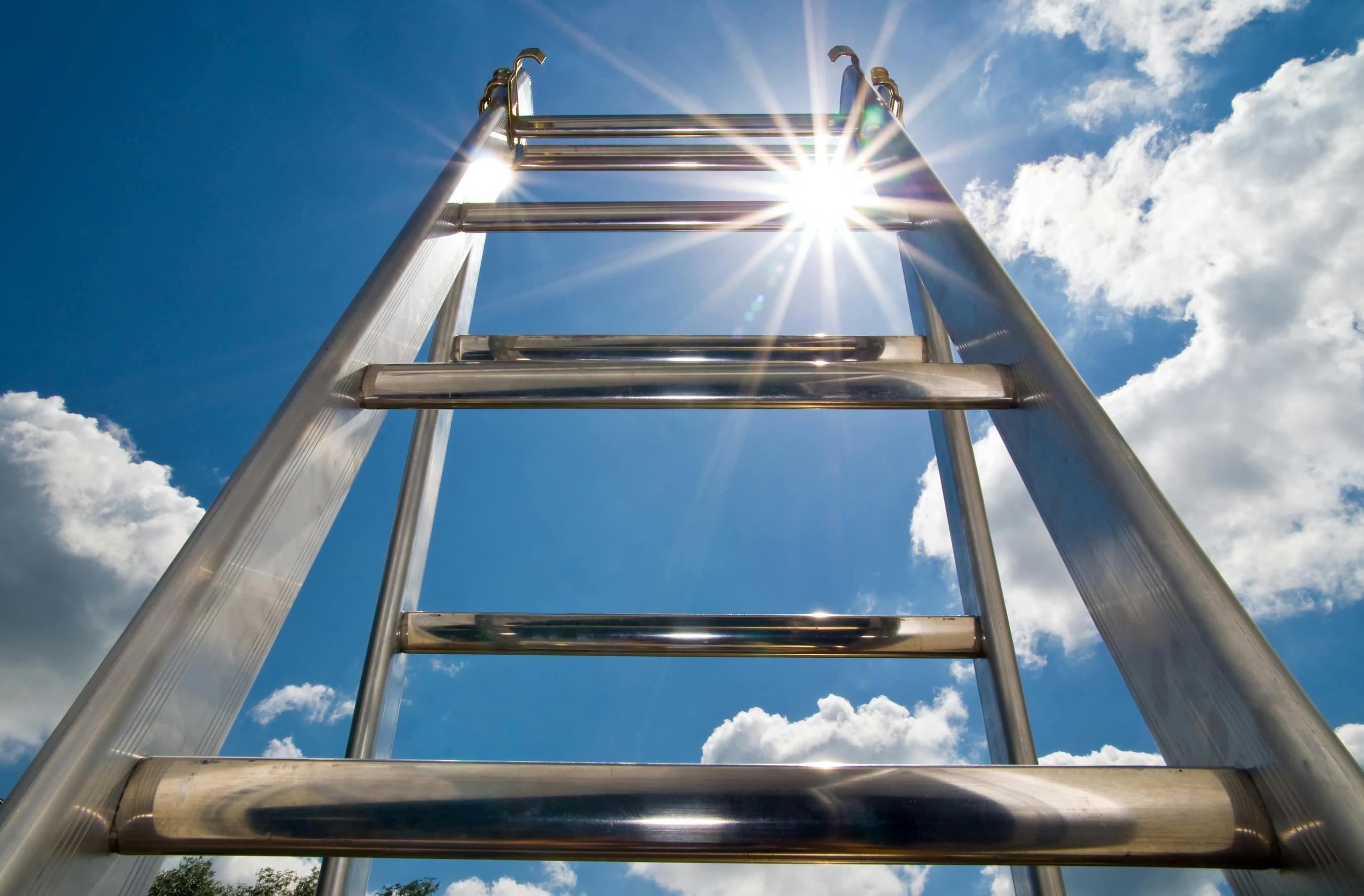 close-up picture of aluminum ladder with a blue sky, sunshine and clouds in the background