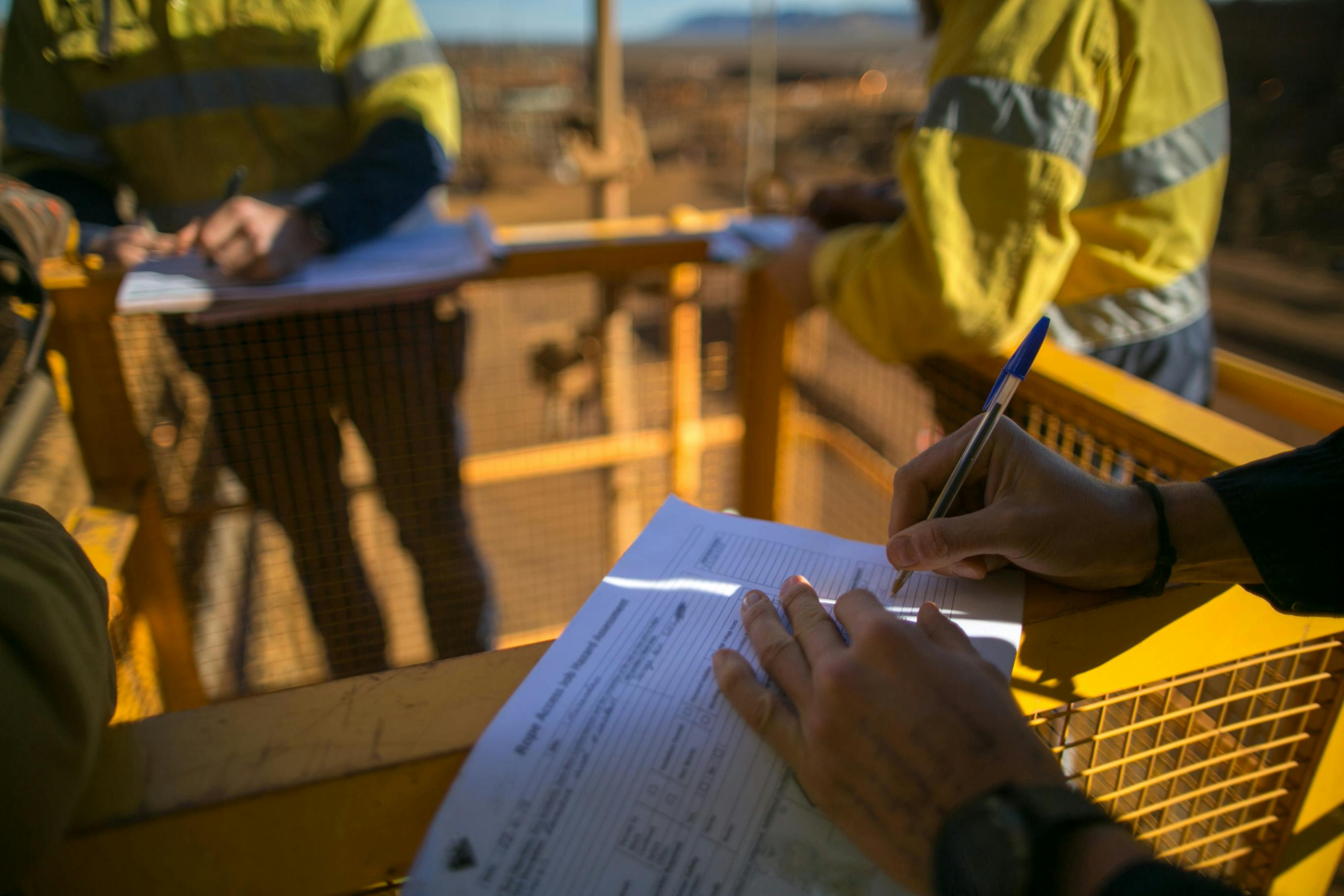 Workers out in the field wearing hi-vis jackets and filling out job hazard analysis paperwork