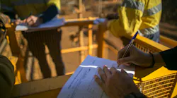 Workers out in the field wearing hi-vis jackets and filling out job hazard analysis paperwork Workers out in the field wearing hi-vis jackets and filling out job hazard analysis paperwork