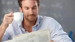 man sitting and holding an espresso cup in one hand and the newspaper in another man sitting and holding an espresso cup in one hand and the newspaper in another