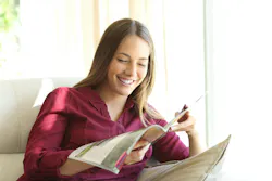 Woman smiling and sitting on a beige couch reading a magazine Woman smiling and sitting on a beige couch reading a magazine