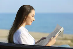 woman reading the newspaper outside on a bench near the beach woman reading the newspaper outside on a bench near the beach