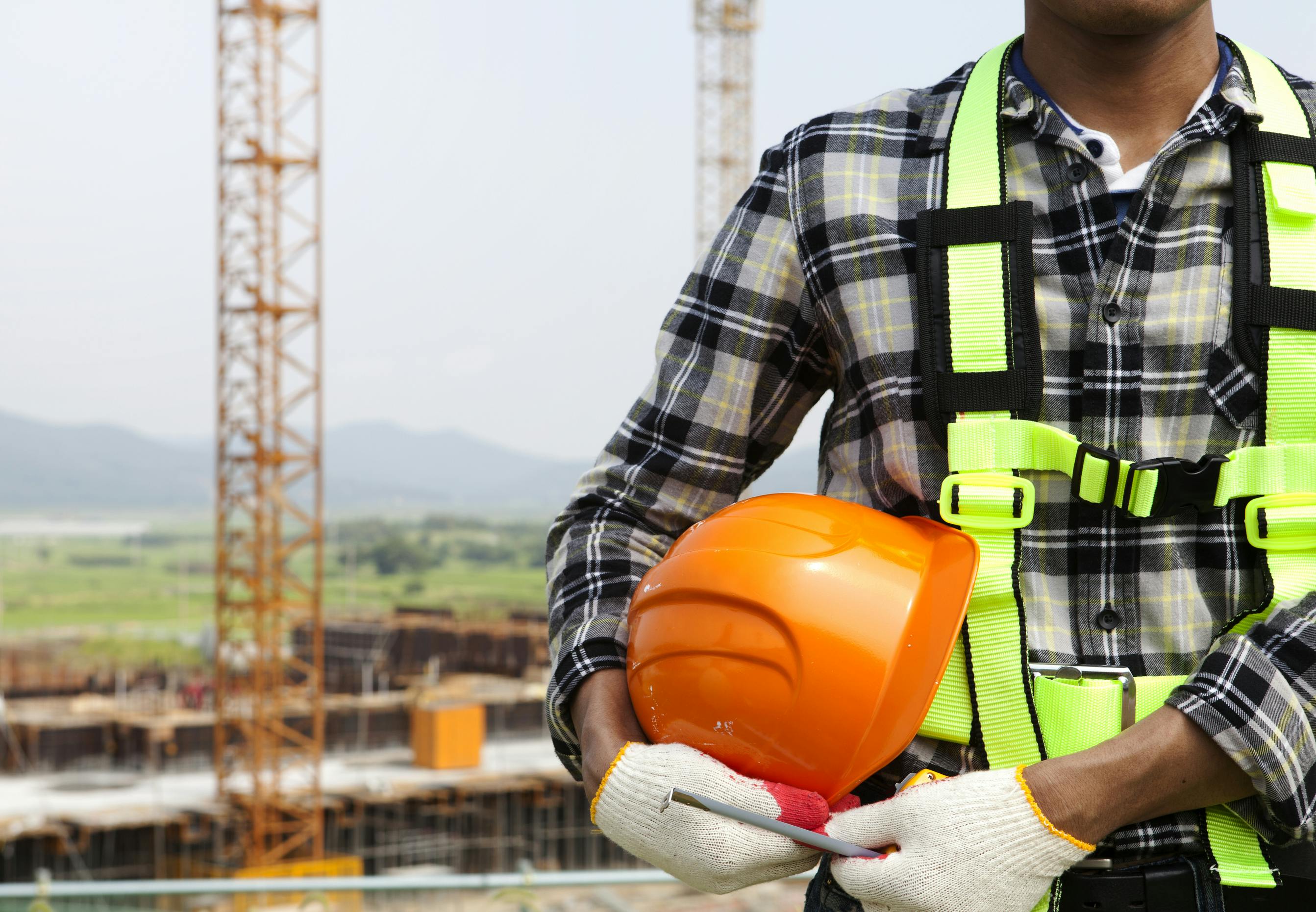 picture of construction worker wearing hi-vis vest and gloves holding a hard hat