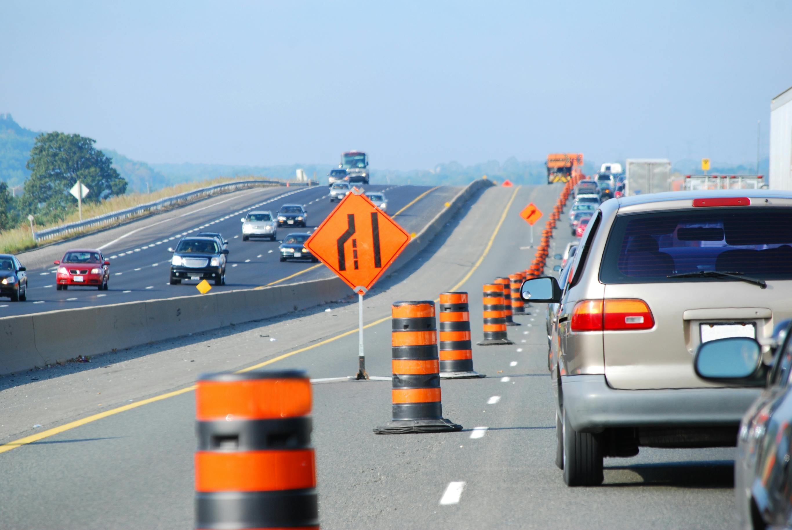 picture of cars bumper to bumper on a highway with one lane closed for construction, with signage