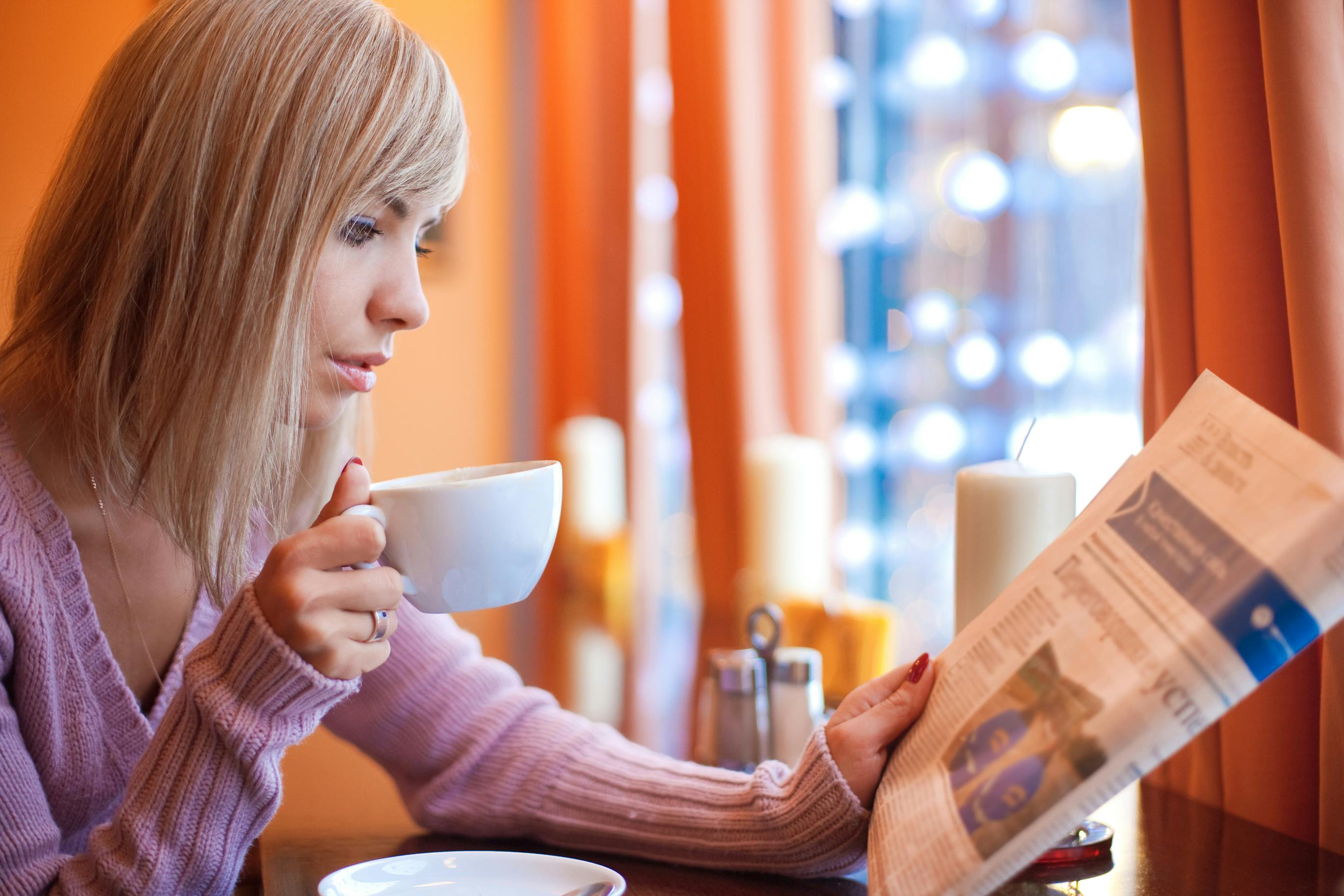 picture of young woman holding a newspaper in one hand and coffee mug in the other