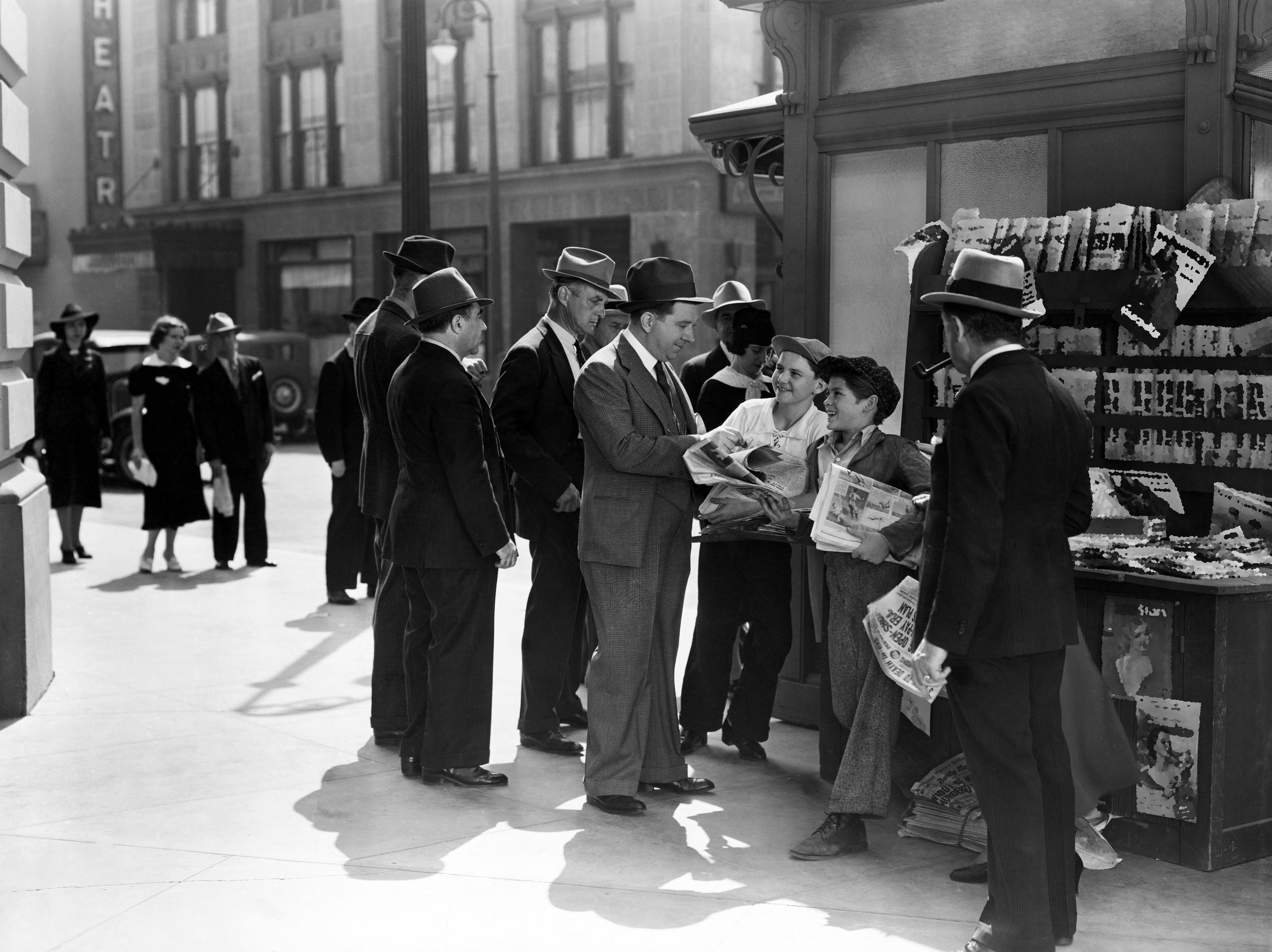 black and white photo of men and boys gathered around a newsstand holding newspapers