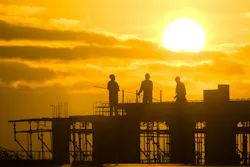 picture of three construction workers atop a framed structure with the sun in the background