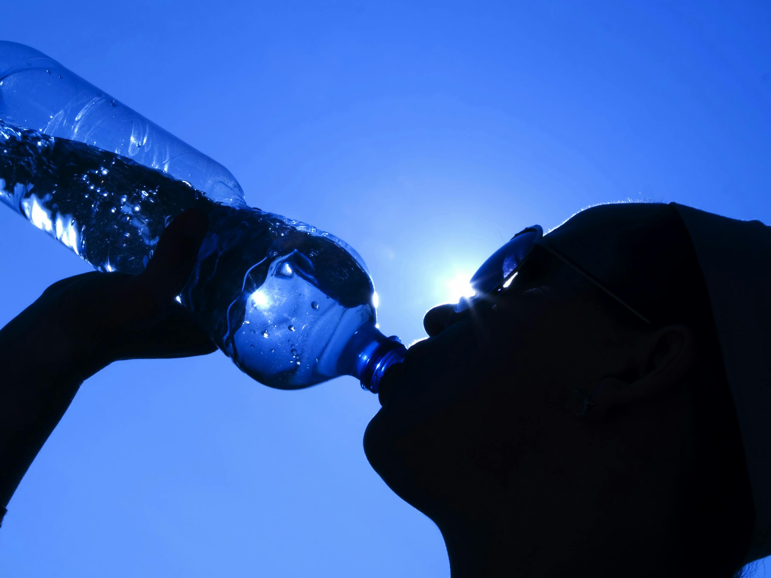 silhouette of woman drinking water against a blue sky, representing heat wave and OSHA's new proposed heat safety standard