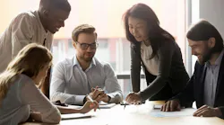 picture of five employees huddled around a table in an office setting. A conceptual representation of employee engagement.